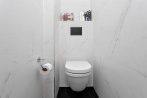 a white bathroom with a toilet and a toilet paper dispenser at Frish & Diz by HolyGuest in Tel Aviv +2 photos