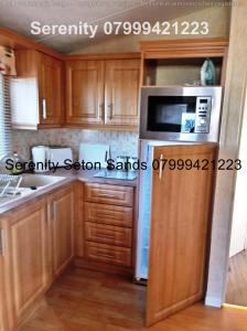a kitchen with wooden cabinets and a microwave at Serenity Seton Sands in Longniddry