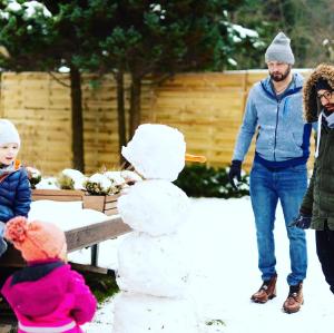 Une famille jouant avec un bonhomme de neige dans la neige dans l'établissement Chata Pod Lasem, à Poręba