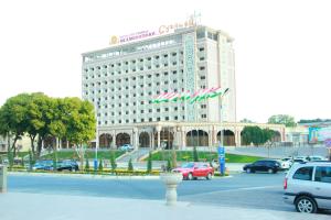 a large white building with cars parked in a parking lot at Sugdiyon Hotel in Khujand