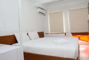 ein weißes Schlafzimmer mit 2 Betten und einem Fenster in der Unterkunft Comfy Studio Room at Patraland Urbano Apartment By Travelio in Bekasi