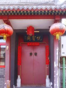 czerwone drzwi budynku z dwoma czerwonymi latarniami w obiekcie Beijing Yue Bin Ge Courtyard Hotel w Pekinie