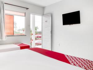 a white bedroom with two beds and a flat screen tv at OYO Praia Hotel Recanto do Tomé - Salvador in Paripe