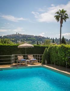 a swimming pool with two chairs and an umbrella at Hôtel & Restaurant Alain Llorca in La Colle-sur-Loup