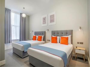 two beds in a hotel room with orange pillows at Townhouse Apollo, Hyde Park in London