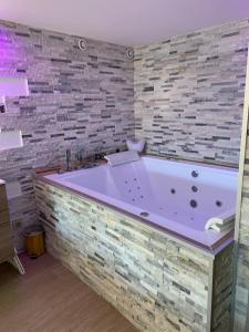 een groot paars bad in een badkamer met een stenen muur bij Le Menhir Jacuzzi Lit 200x200 in Le Cendre