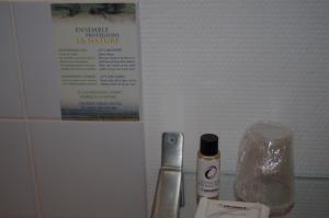 a bathroom counter with a bottle of lotion and a sign at The Originals City, Hôtel Le Savoy, Caen (Inter-Hotel) in Caen