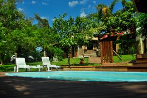 two white chairs sitting next to a swimming pool at Pousada Dormida do Peixe in Praia do Rosa