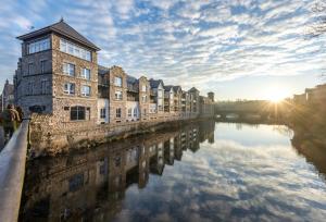 a row of buildings next to a river with the sunset at Luxury riverside apartment in Kendal in Kendal