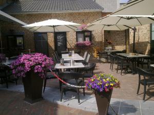 un patio con tavoli, sedie, fiori e ombrelloni di B&B de Taller-Hoeve a Maasmechelen