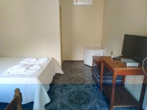 a room with a bed and a desk with a television at Estalagem São Gonçalo in Tarituba