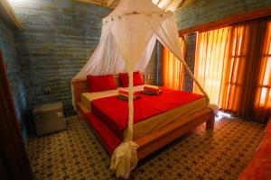 sypialnia z czerwonym łóżkiem z baldachimem w obiekcie Segar Village w Gili Air