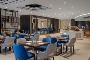 Hyatt Place Dubai Jumeirah في دبي: مطعم فيه كراسي زرقاء وطاولات وبار