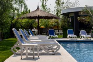 eine Reihe von Liegestühlen und einem Sonnenschirm neben einem Pool in der Unterkunft Hotel Los Alpes Cipreses in Asunción