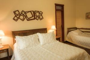 um quarto com uma cama branca, um espelho e uma cama lateral. em Pousada Encanto da Serra em Tiradentes