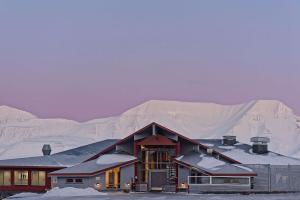 uma casa na neve com uma montanha ao fundo em Radisson Blu Polar Hotel, Spitsbergen em Longyearbyen