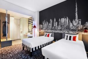 ibis Styles Dubai Airport Hotel في دبي: غرفة فندقية بسريرين ولوحة على الحائط