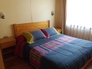 a bedroom with a bed with colorful sheets and a window at Cabañas Amancay in Puerto Varas