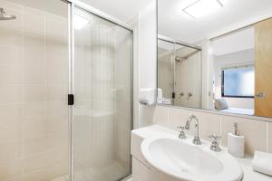 a white bathroom with a sink and a shower at Beach Club Resort Mooloolaba in Mooloolaba