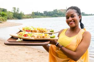 a woman holding a tray of food on the beach at Kivu Paradis Resort in Nyamyumba
