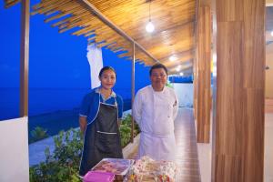 Seamount Hotel Amed في آميد: رجلان واقفان في مطبخ مع طاولة مع طعام