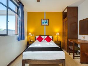 1 dormitorio con cama con almohadas rojas y escritorio en Capital O Parador Crespo Hotel, Oaxaca en Oaxaca de Juárez