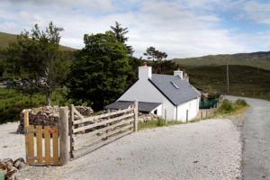 a small white house with a fence next to a road at Glas Bheinn Cottage in Luib