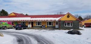a yellow building with a red roof in the snow at Middlebury Sweets Motel in Middlebury