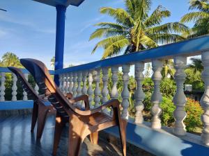 a rocking chair on a balcony with palm trees in the background at Morjim Sunset Guesthouse - 300 meter to Morjim Beach in Morjim