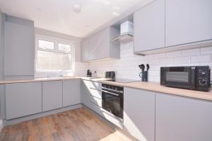a white kitchen with white cabinets and a microwave at Queens Quarter Townhouse 1 in Belfast