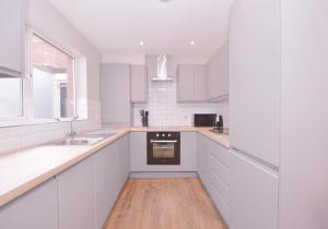 a white kitchen with white cabinets and a wooden floor at Queens Quarter Townhouse 2 in Belfast
