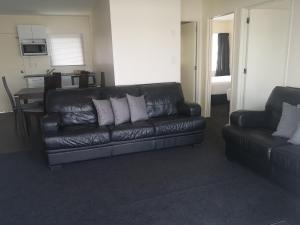 a living room with a leather couch and a kitchen at Twin Coast Adventures in Kaikohe