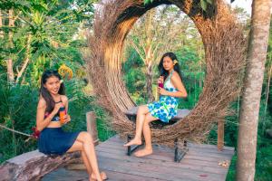dwie młode kobiety siedzące na ławce w wiklinowym łuku w obiekcie Mirah Guest House w mieście Tampaksiring