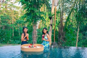 due donne in piedi in acqua vicino a una piscina di Mirah Guest House a Tampaksiring