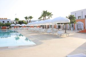 a pool with white umbrellas and tables and chairs at Villetta Residence Chiusurelle in Porto Cesareo