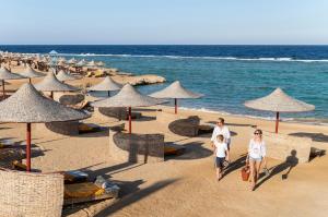 mężczyzna i kobieta spacerujący po plaży z parasolami w obiekcie Three Corners Happy Life Beach Resort w mieście Abu Dabbab