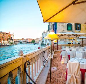 威尼斯的住宿－帕拉佐斯特恩酒店，一间位于水边的餐厅,配有桌子和遮阳伞