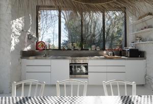 una cocina con armarios blancos y sillas y ventanas blancas. en Casa Candela, en Posada