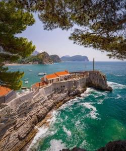 a house on a cliff next to the ocean at Apartments Teodora Obala in Petrovac na Moru
