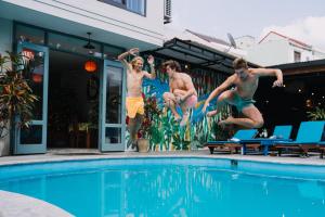 three young men jumping into a swimming pool at Bed Station Hostel & Pool Bar Hội An " Former Sunflower" in Hoi An