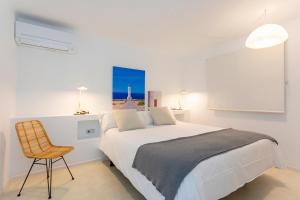 ein weißes Schlafzimmer mit einem Bett und einem Stuhl in der Unterkunft Apartamentos Roca Plana in Es Pujols