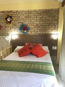 a bed with two red pillows and a brick wall at Pousada Beija-Flor in Bombinhas