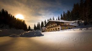 a building in the snow with the sun in the background at Hotel Dolomiti Des Alpes in Misurina