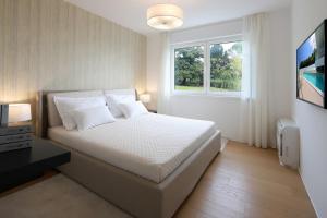 a white bedroom with a bed and a window at New apartment with swimming pool near the beach in Ičići