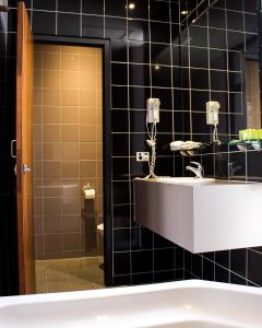 a black tiled bathroom with a sink and a tub at Highlander Hotel Bar Kitchen Rooftop in Adelaide