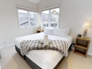 a bedroom with a large white bed with two windows at Family Chalet 33 The Stables Perisher in Perisher Valley