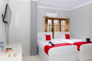 two beds in a white room with red pillows at RedDoorz Plus near Transmart Kairagi Dua manado in Manado