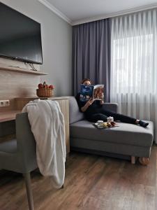 une femme assise sur un canapé qui lit un livre dans l'établissement Hotel Cristal, à Nuremberg