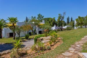 um jardim com palmeiras e uma casa ao fundo em Prado do Golf em Vilamoura