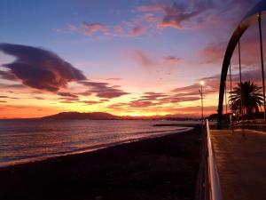a sunset over a beach with a palm tree and the ocean at El Nogal Home in Málaga